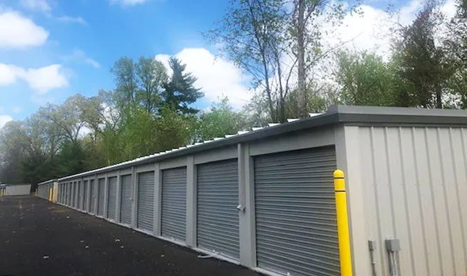 Row of gray storage units under a bright blue sky with trees in the background